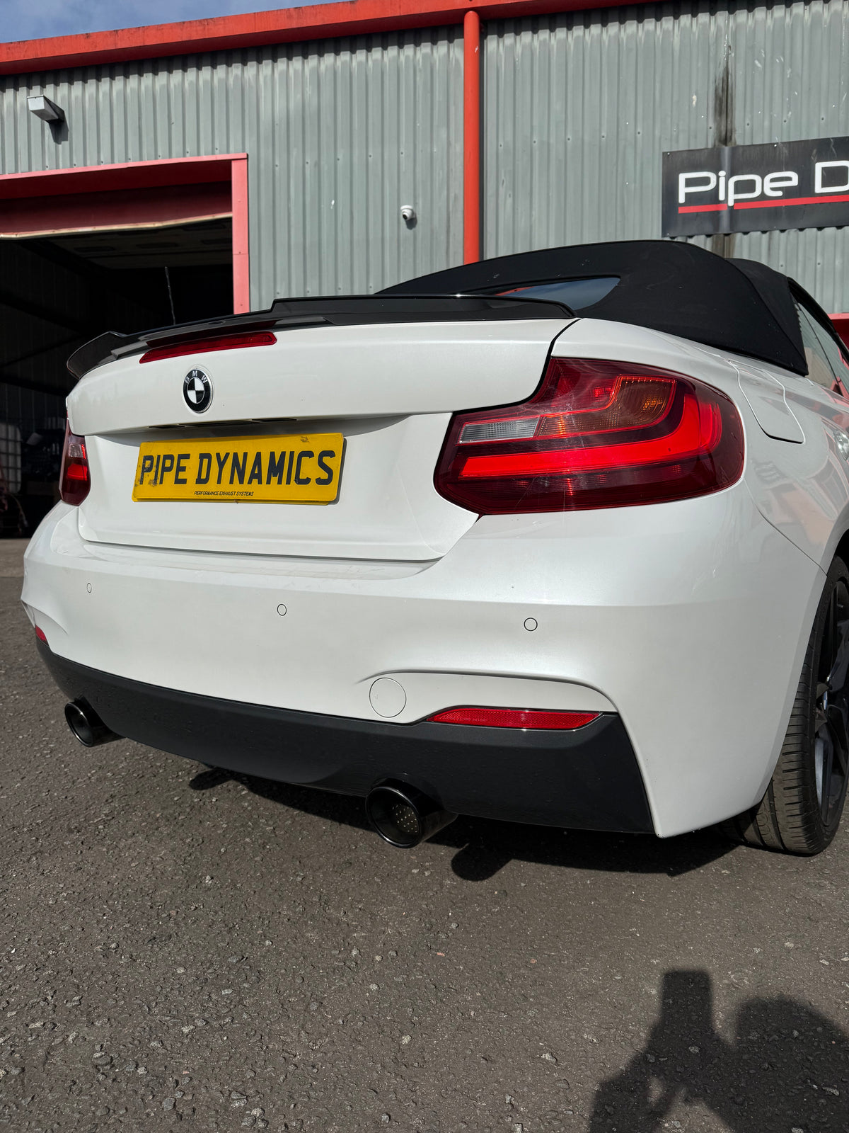 White BMW 2 Series 220d Convertible rear view with a black soft top, black diffuser, and a PIPE DYNAMICS EXHAUST